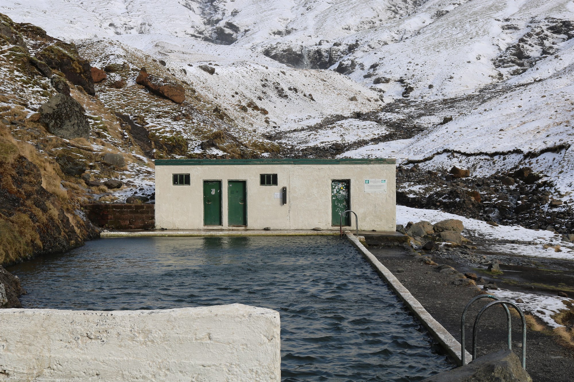 Seljavallalaug hot spring with changing facilities surrounded by rocky Iceland landscapes.